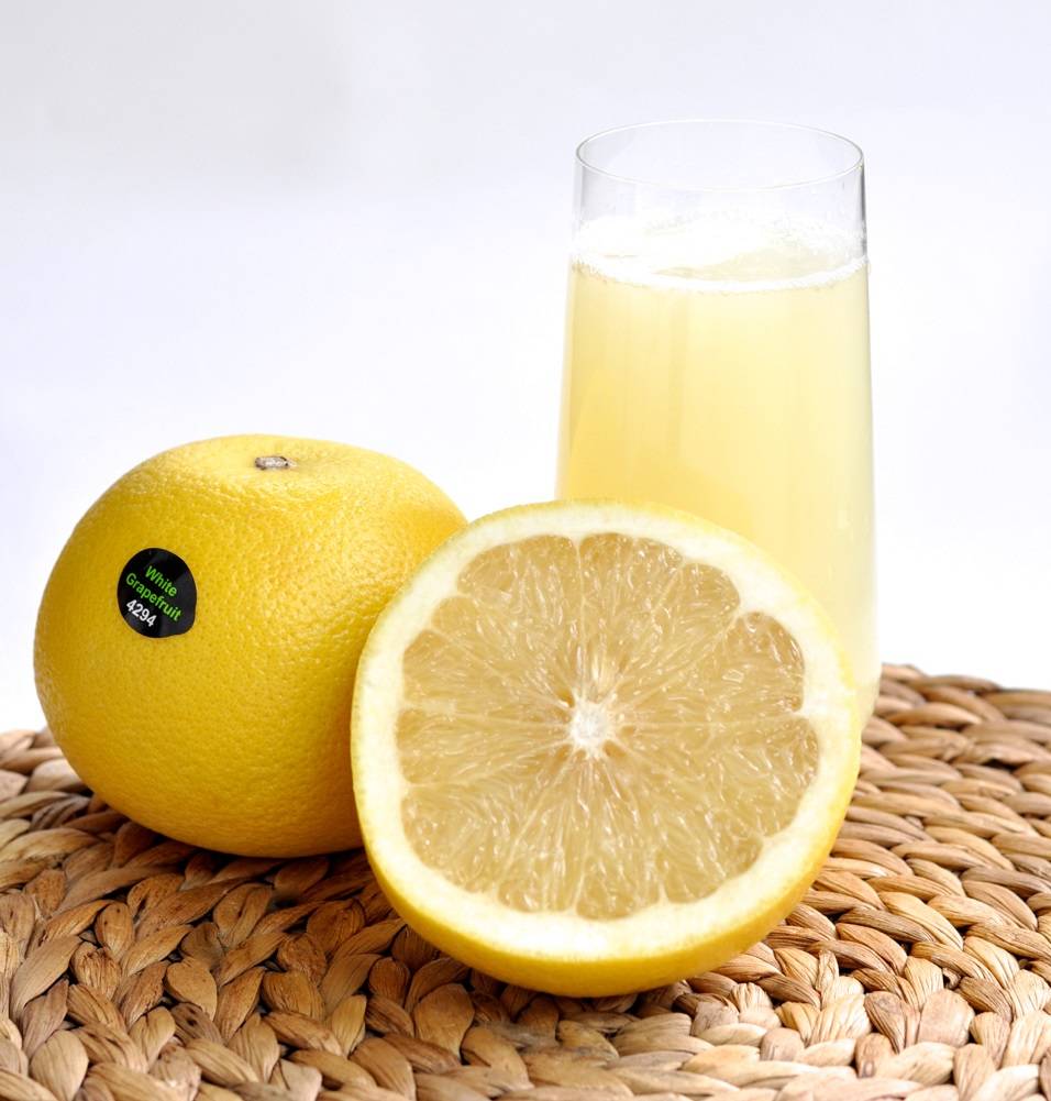 Weiße Jaffa Grapefruit aus Israel, aufgeschnitten mit hellem saftigem Fruchtfleisch, daneben ein Glas frischer Grapefruitsaft